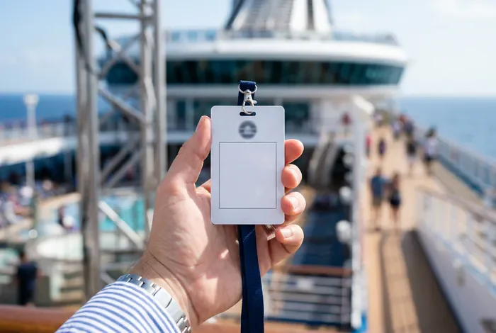 Travailler sur un bateau de croisière : Le guide 2026 - Travailler sur un bateau de croisière : 6 étapes pour réussir - Voulez-vous travailler sur un bateau de croisière en 2026 ? Badge d'identification de membre d'équipage devant un navire de croisière.