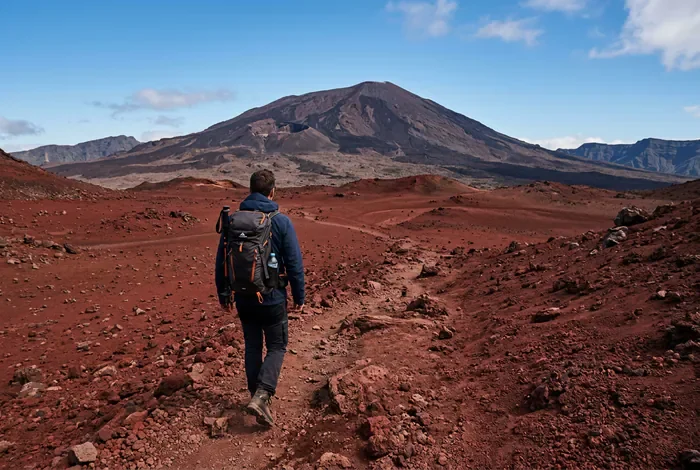 Randonnée au Piton de la Fournaise : Guide 2026 - Piton de la Fournaise : Le Guide Ultime Randonnée - Comment réussir la randonnée au Piton de la Fournaise ? Randonneur marchant sur le sol rouge désertique de la Plaine des Sables