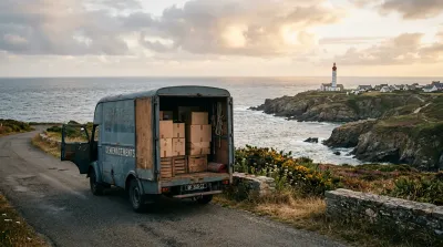 Un camion de déménagement garé face à la mer en Bretagne avec un phare en arrière-plan, symbolisant le nouveau départ.